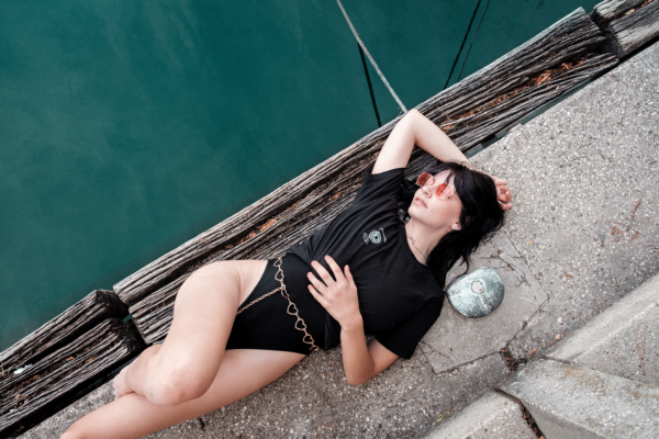 A woman wearing a black "Onlyfans" shirts is laying on a dock.