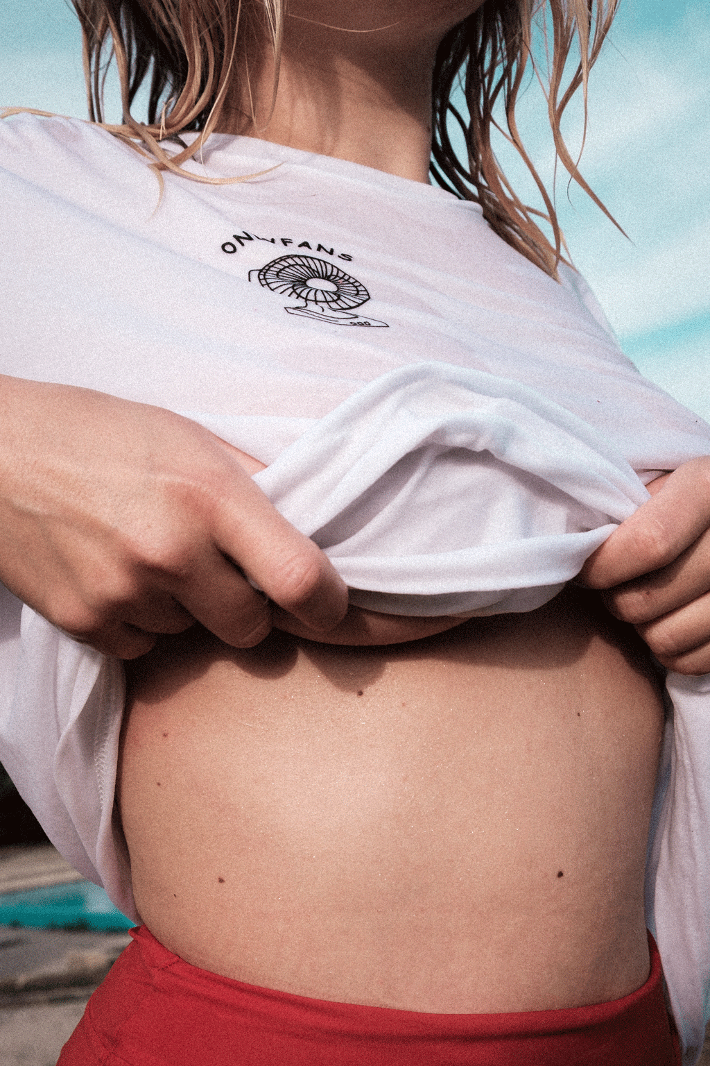 A woman with red bikini shorts, slightly lifting her wet "onlyfans" shirt. Her face is cropped.