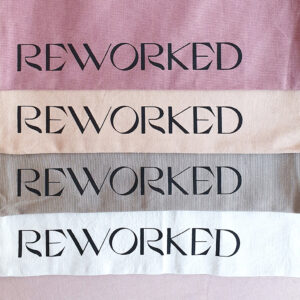 Four different colored tote-bags from Reworked, stacked on a pink sofa.