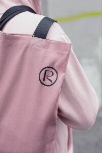 Closeup of a dark pink "reworked" bag, resting on top of someones shoulder. The person is wearing a pastel pink hoodie.